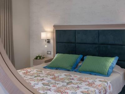 Schlafzimmer mit Doppelbett, grünen Kissen, Teppich und Nachttischlampen in einem Hotelzimmer.