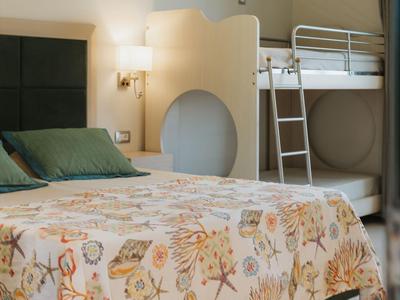 Hotelzimmer mit Doppelbett und Etagenbett, hell, mit Lampen und Vorhängen.