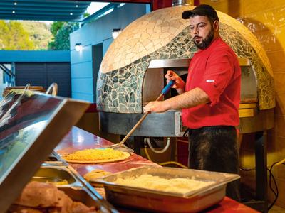 Muž v červené košili používá lopatu k vyjmutí pizzy z dřevěné pece v pizzerii.