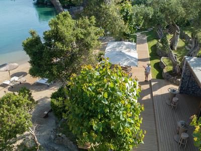 Vista de un área de descanso sombreada con sombrillas en el jardín de un hotel junto al agua.