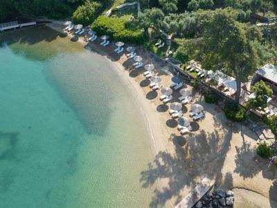 Strand mit Sonnenschirmen und Liegestühlen neben klarem, türkisfarbenem Wasser und grüner Vegetation.