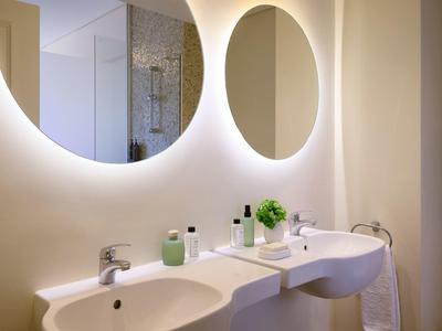 Moderner Badezimmerspiegel mit indirekter Beleuchtung über zwei Waschbecken und weißen Armaturen.