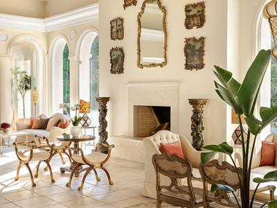 Salón elegante con paredes blancas, espejo sobre la chimenea y asientos elegantes.