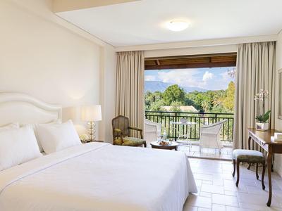 Helles Hotelzimmer mit großem Bett, Balkon und Blick auf grüne Natur.