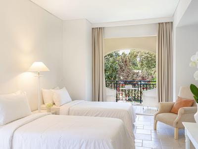 Helles Hotelzimmer mit zwei Einzelbetten und Balkon mit Blick ins Grüne.