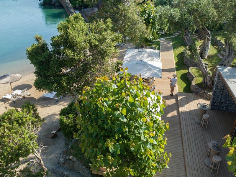 Blick auf eine Terrasse mit Sonnenschirm und Sitzgelegenheiten an einem grünen, bewachsenen Ort nahe Wasser.