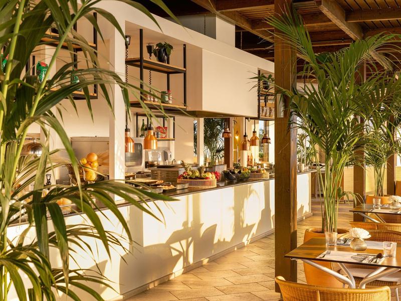 Moderne Hotellounge mit Buffetbereich, Pflanzen und gedeckten Tischen in warmem Licht.