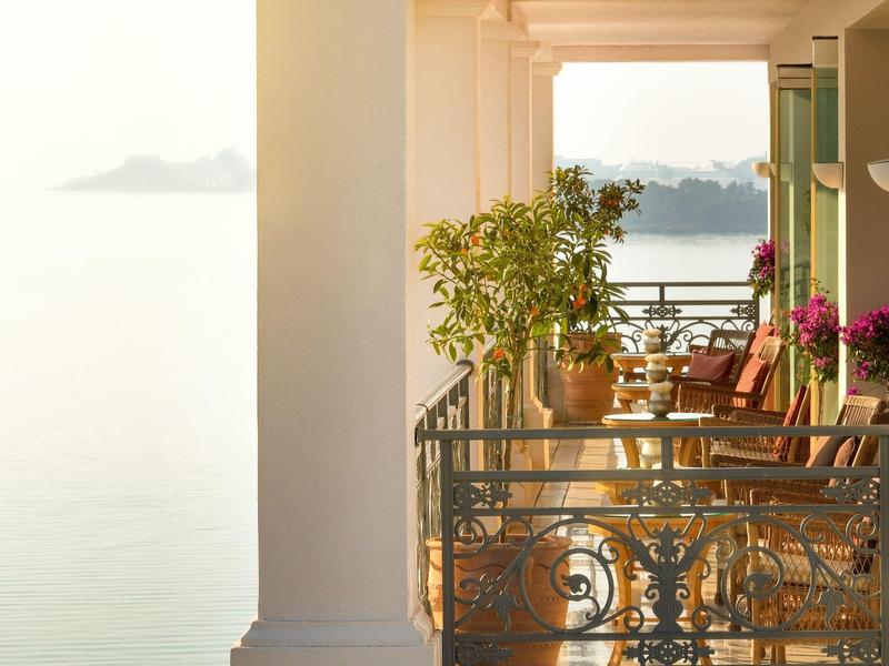 Balkon mit Stühlen, Tischen und Pflanzen mit Blick auf das Meer bei Sonnenuntergang.