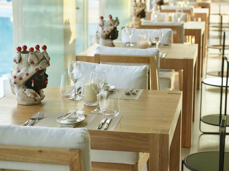 Restaurant mit Holztischen, weißen Stühlen und dekorativen Figuren am Fenster.