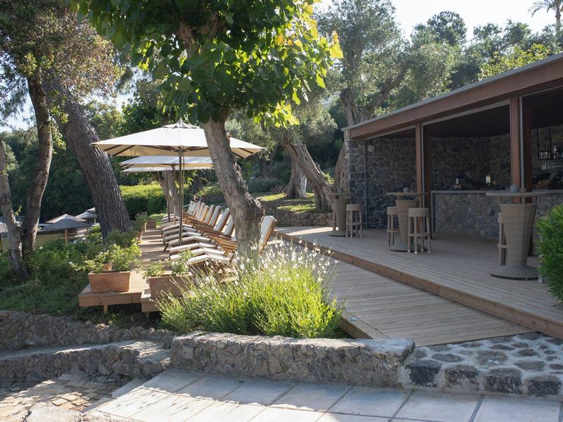 Terrasse mit Sitzgelegenheiten vor einem Gebäude, umgeben von Bäumen und Pflanzen
