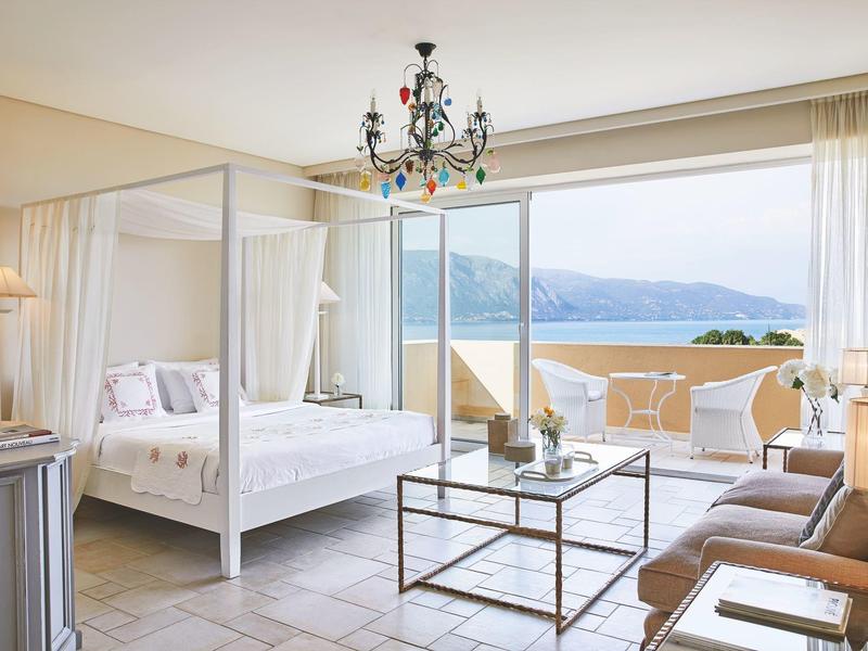Helles Hotelzimmer mit Himmelbett, Sitzecke und Balkon mit Meerblick.