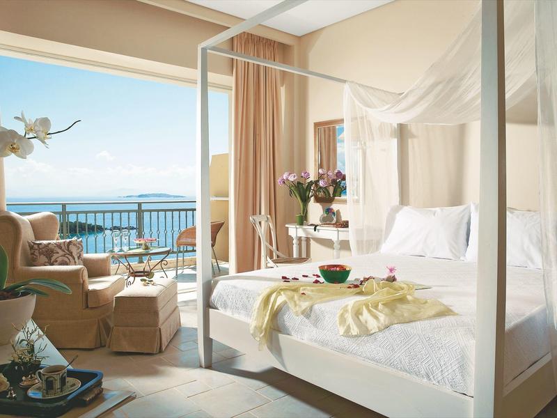 Elegantes Hotelzimmer mit Himmelbett, Sitzbereich und Meerblick auf Balkon.