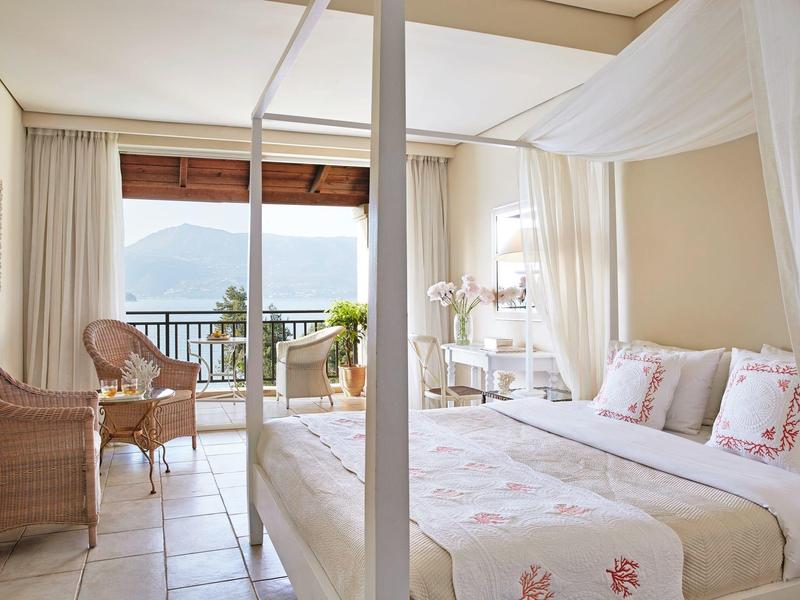 Helles Hotelzimmer mit Himmelbett, Rattanstühlen und Balkon mit Bergblick.