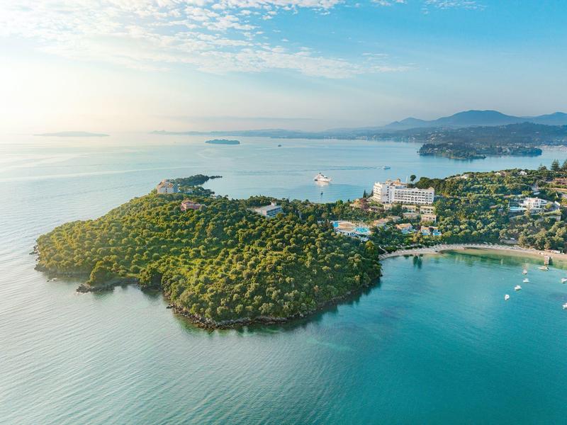 Luftaufnahme einer bewaldeten Halbinsel mit Strand und Hotelanlagen am Meer.