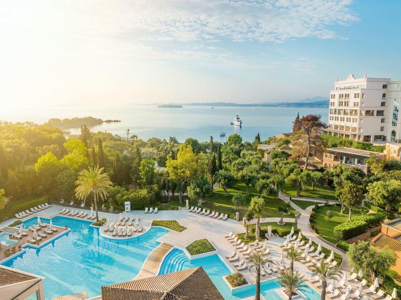 Hotelpool mit Liegestühlen und Blick auf das Meer bei Sonnenaufgang.
