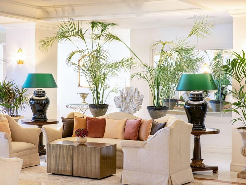 Helle Lounge mit cremefarbenen Sofas, grünen Lampen und vielen Zimmerpflanzen.