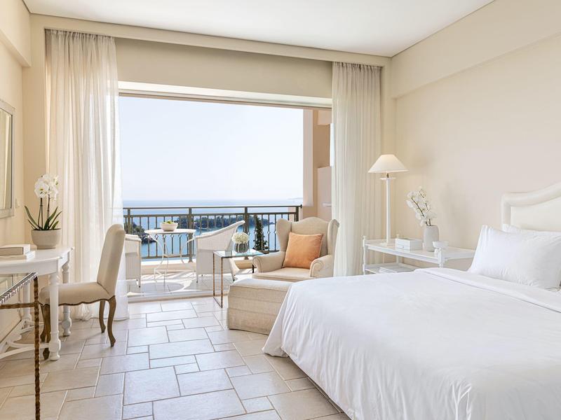 Helles Hotelzimmer mit Doppeltbett, Sitzbereich und Balkon mit Meerblick.