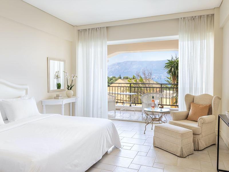 Helles Hotelzimmer mit großem Bett, Sessel und Balkon mit Bergblick.