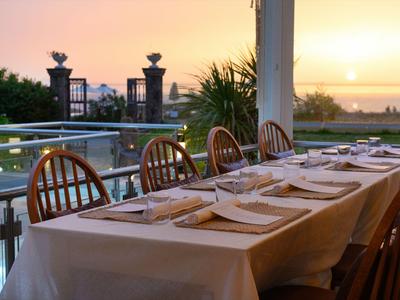 Ein gedeckter Tisch auf einer Terrasse mit Blick auf den Sonnenuntergang am Meer.