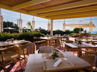 Überdachte Terrasse eines Restaurants mit gedeckten Tischen und Blick auf das Meer bei Sonnenaufgang.