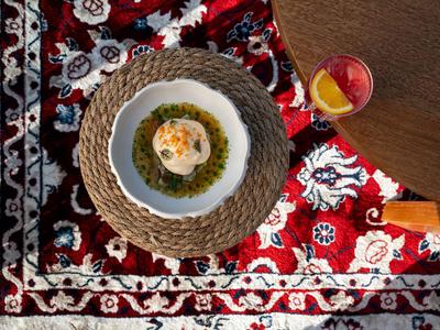 Vogelnest förmiges Gericht auf grünem Püree mit orangefarbenem Getränk auf Teppich