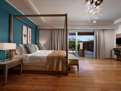 Hell eingerichtetes Hotelzimmer mit Himmelbett, Holzboden und Balkon mit Meerblick.