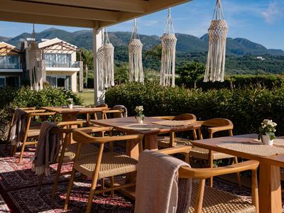 Gemütliche Außenterrasse mit Holzmöbeln und Blick auf grüne Hügel unter blauem Himmel.