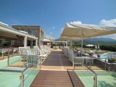 Holzsteg zum Poolbereich eines Hotels mit weißen Sonnenschirmen und Bergblick.