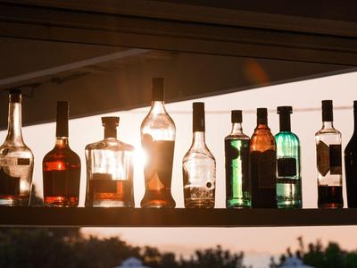 Verschiedene Spirituosenflaschen stehen auf einem Regal mit Sonnenlicht im Hintergrund.