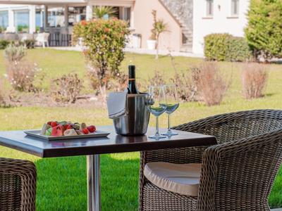 Terrasse mit zwei Stühlen, Tisch mit Wein und Glas, Blick auf modernes Haus und Garten.