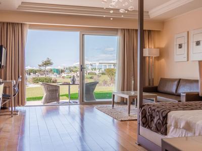 Hotelzimmer mit Doppelbett und Blick auf eine Terrasse und Poollandschaft im Freien.