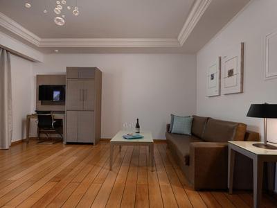 Modern eingerichtetes Hotelzimmer mit braunem Sofa, weißem Tisch und Holzboden.