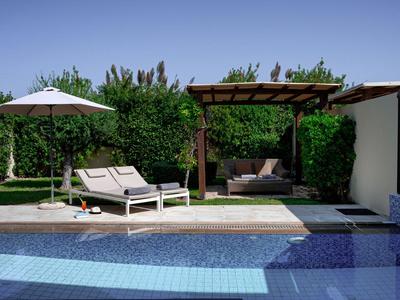 Liegstühle mit Sonnenschirm neben Pool und Lounge-Bereich im Garten eines Hotels.