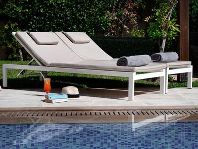 Zwei weiße Liegestühle mit grauen Handtüchern neben einem Pool, umgeben von grünem Garten.