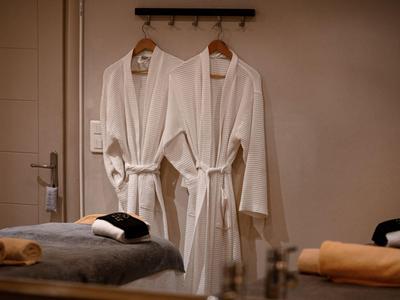 Zwei weiße Bademäntel hängen an einer Wand in einem Spa- oder Wellnessbereich.