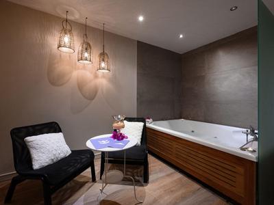 Zimmer mit Badewanne, zwei Stühlen, kleinem Tisch und drei Hängeleuchten an der Wand.