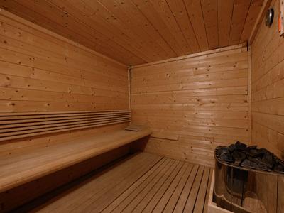 Holzsauna mit Holzbänken und einem Ofen mit Saunasteinen in der Ecke.