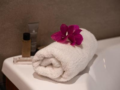 Weißes Handtuch mit einer pinken Orchidee auf einer Badewannenkante mit Seife und Shampoo.