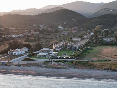 Landschaft mit Strand, Meer, Häusern und Hügeln im Hintergrund bei Sonnenuntergang.