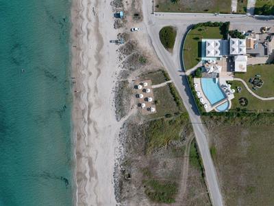 Luftaufnahme eines Hotels mit Pool neben einem Strand mit Sonnenschirmen und Sanddünen.