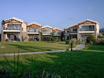 Vier moderne Ferienhäuser mit großen Balkonen und Gartenflächen unter klarem Himmel.
