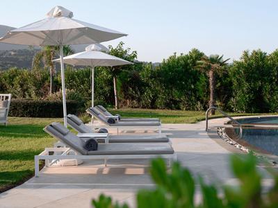 Liegestühle mit Sonnenschirmen neben einem Pool in einer grünen Gartenanlage.