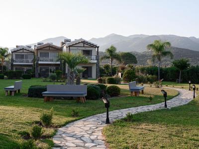 Ein Weg führt durch einen gepflegten Garten zu modernen Ferienhäusern mit Blick auf Berge.