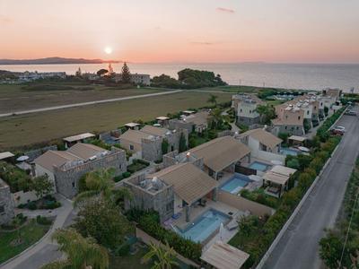 Luftaufnahme einer Küstenanlage mit Villen und Pools am Meer bei Sonnenuntergang.