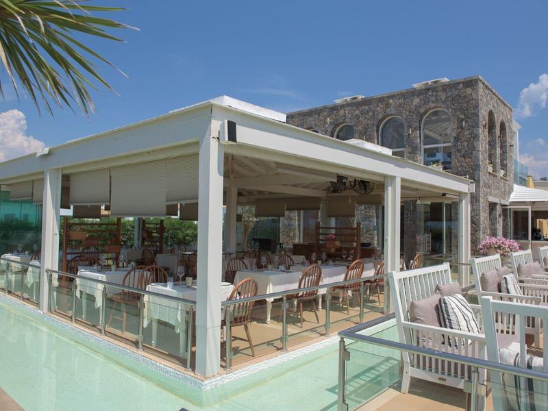 Moderner Außenbereich eines Restaurants mit offenen Seiten und Holzstühlen bei klarem Himmel.