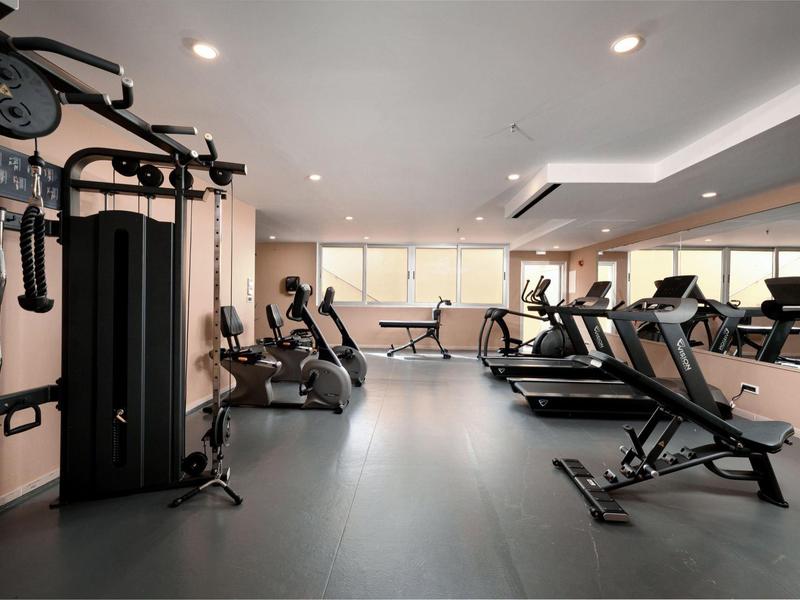 Moderner Fitnessraum mit Laufbändern, Trainingsgeräten und großer Spiegelwand im Hotel.