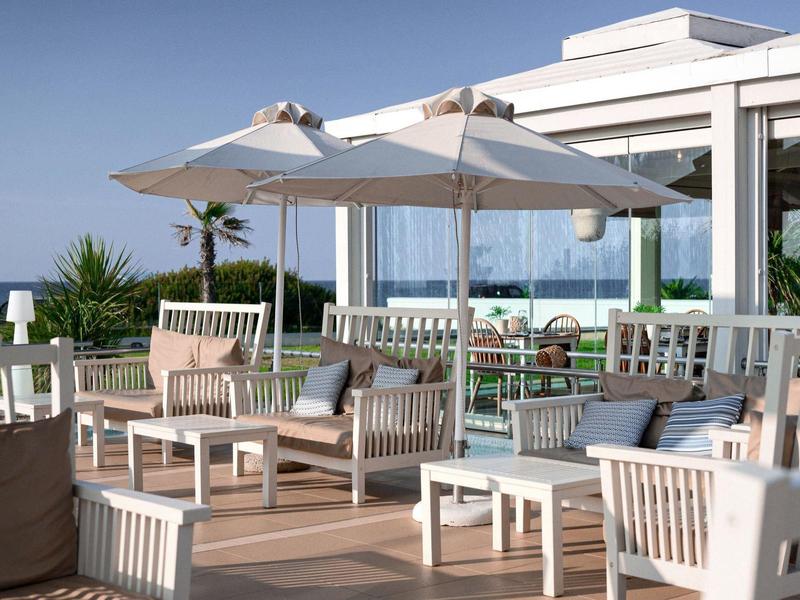 Terrasse mit weißen Holzmöbeln, Sonnenschirmen und Blick aufs Meer