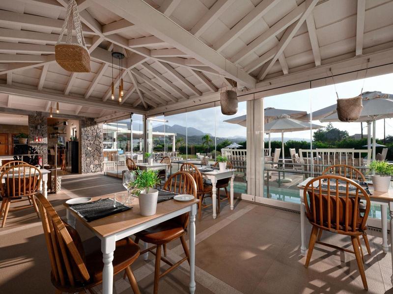 Restaurant mit Holzmöbeln, überdachter Terrasse und Blick auf den Poolbereich.