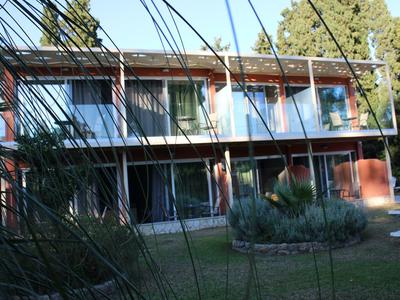 Zweistöckiges Haus mit roter Fassade, großem Garten und Bäumen im Hintergrund bei Sonnenschein.
