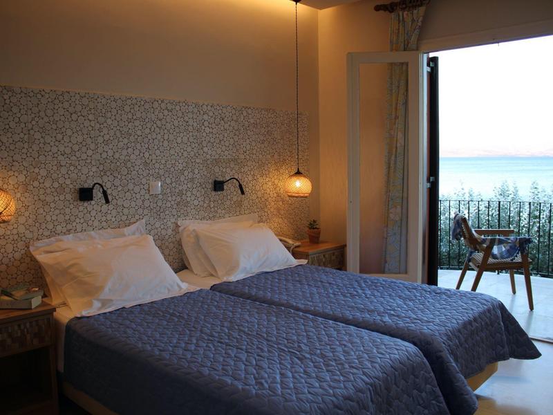 Zweibettzimmer mit blauen Bettdecken, zwei Nachttischen und Zugang zu Balkon mit Aussicht.